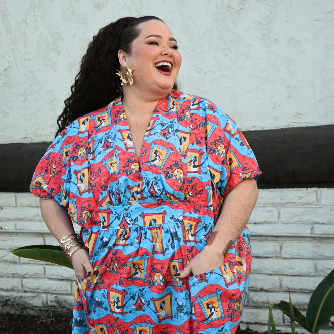 Dark-haired model in red and blue caftan with print of women and birds