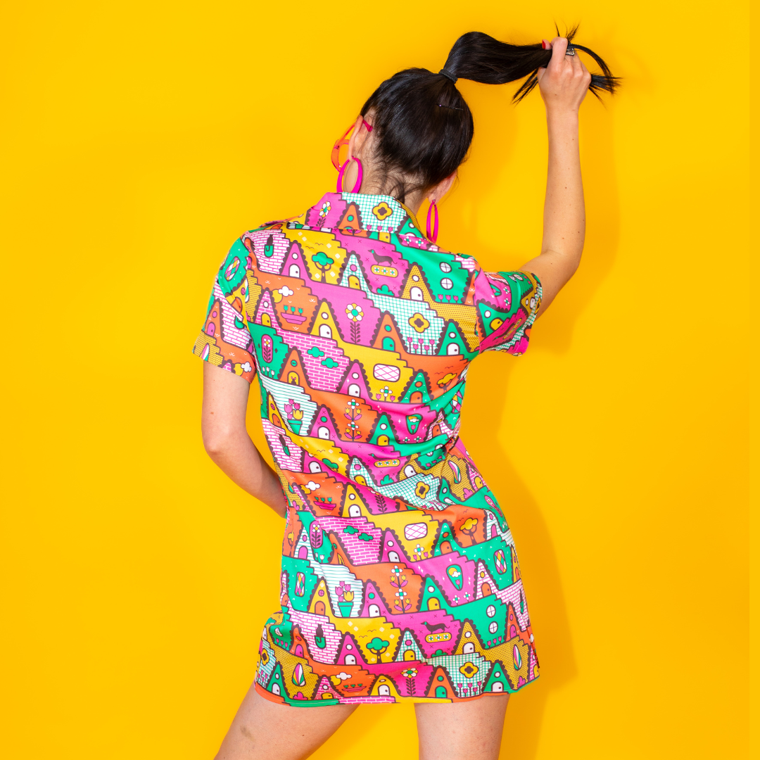 Back view of dark-haired model in bright zip front geometric minidress with white ankle boots and pink sunglasses