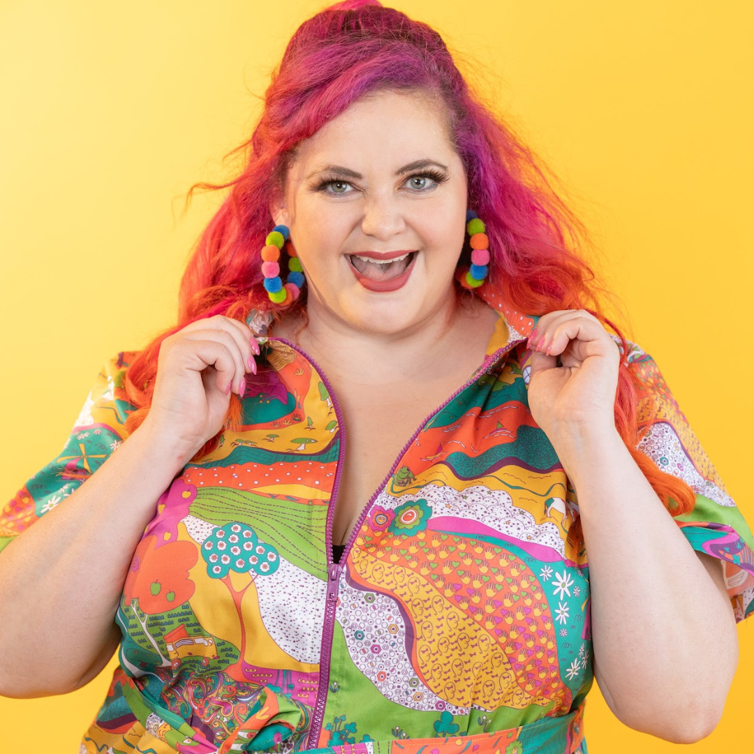 Pink-haired model in brightly colored printed belted minidress, close up, smiling