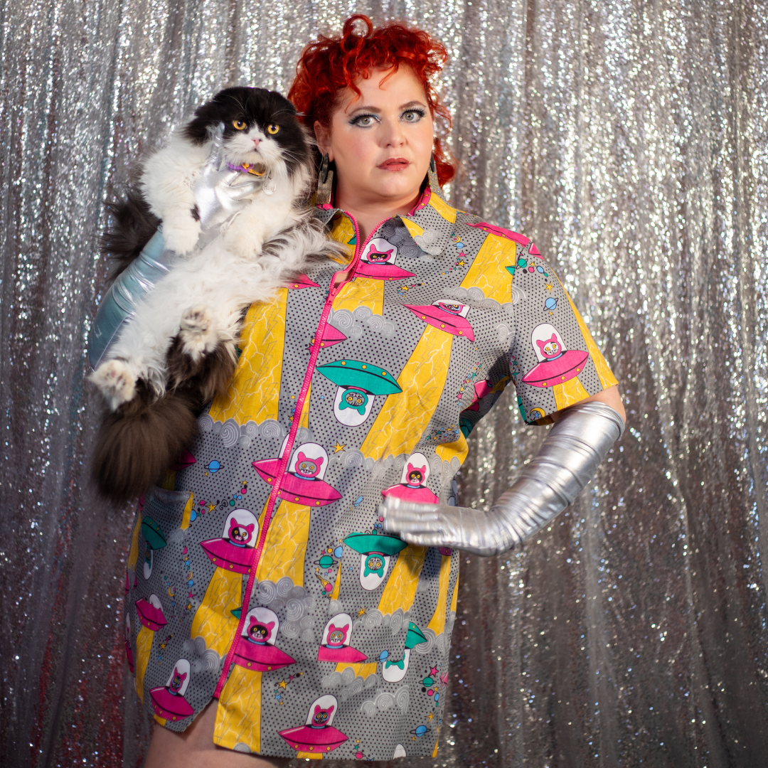 Red-haired model holding cat and wearing minidress with print of cats in spaceships