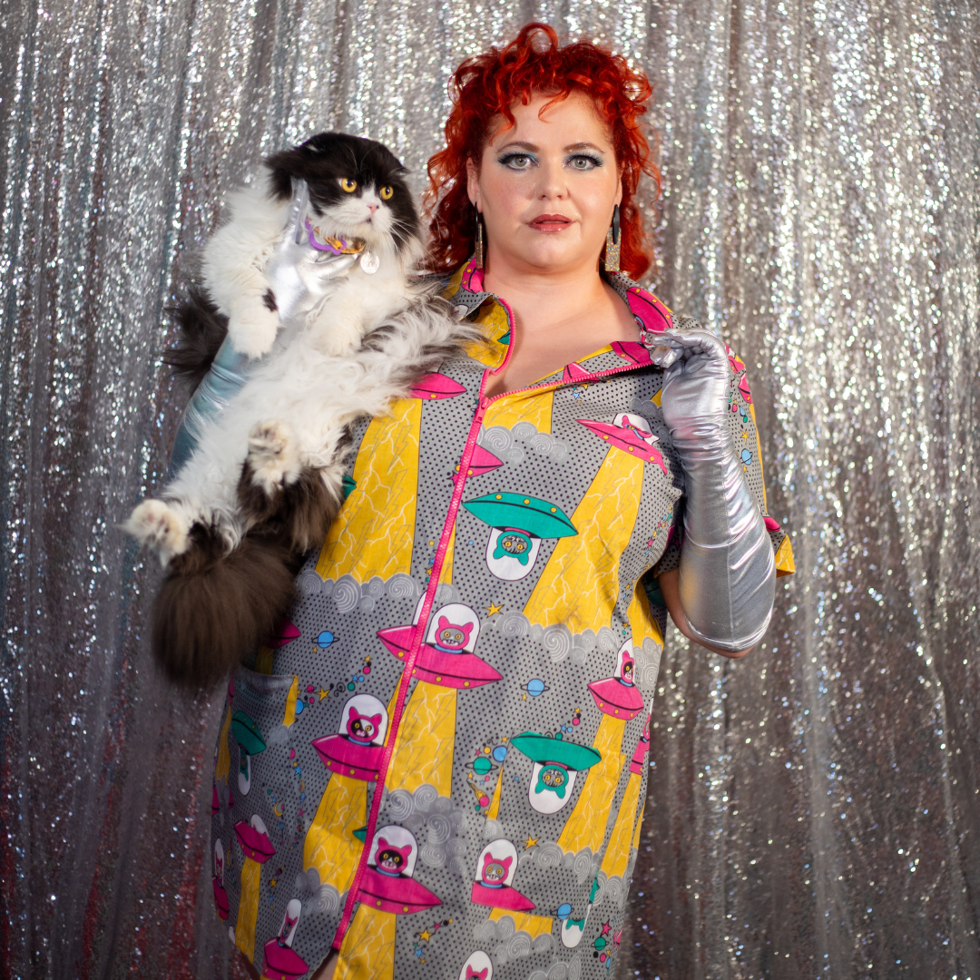 Closeup of red-haired model in collared minidress with space cat print and holding cat