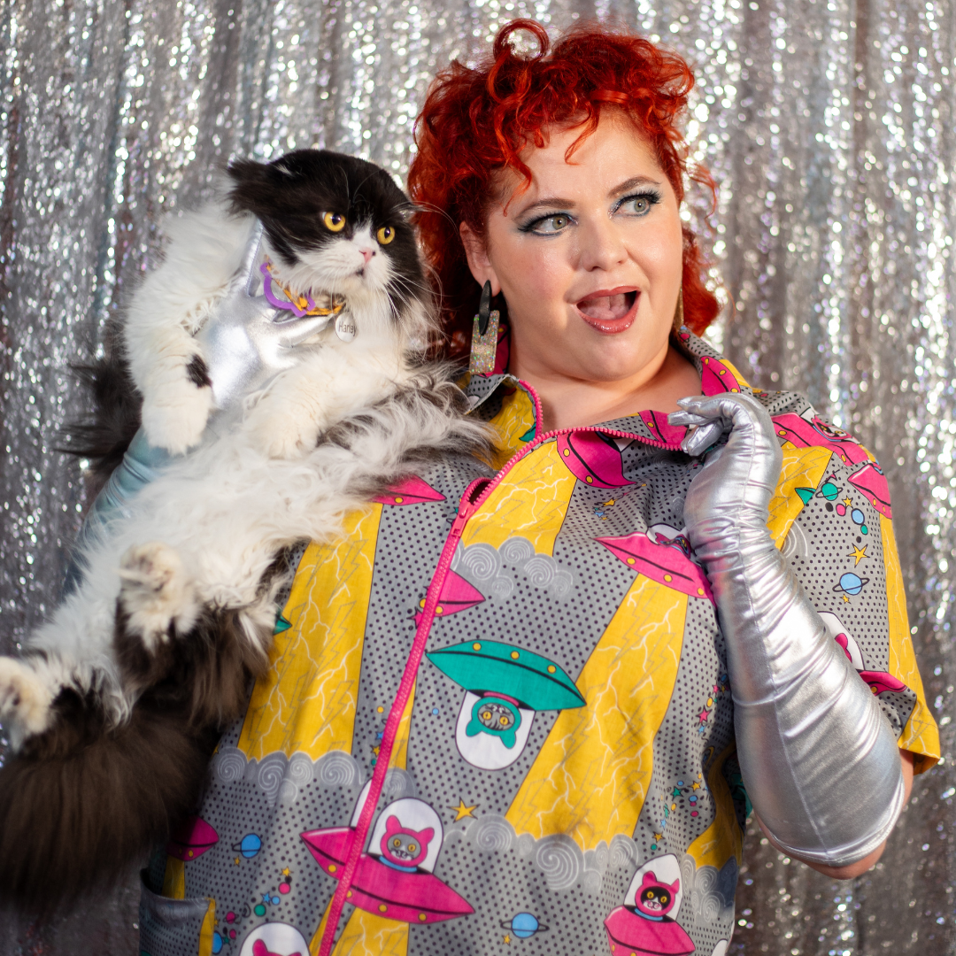 Red-haired model wearing minidress with pink and green spaceships driven by cats