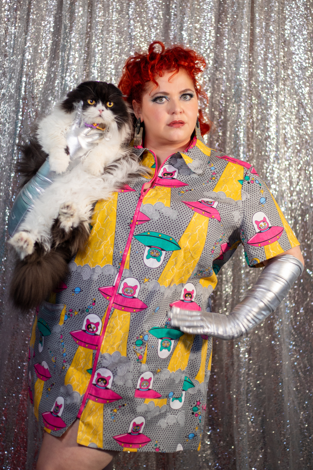 Red-haired model holding cat and wearing minidress with print of cats in spaceships