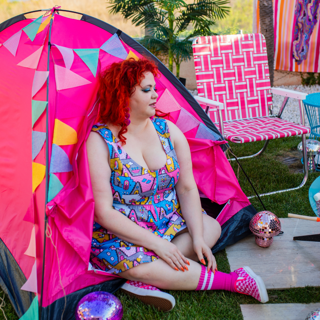 Red-haired model in pastel 80s inspired zip dress and sitting inside bright tent