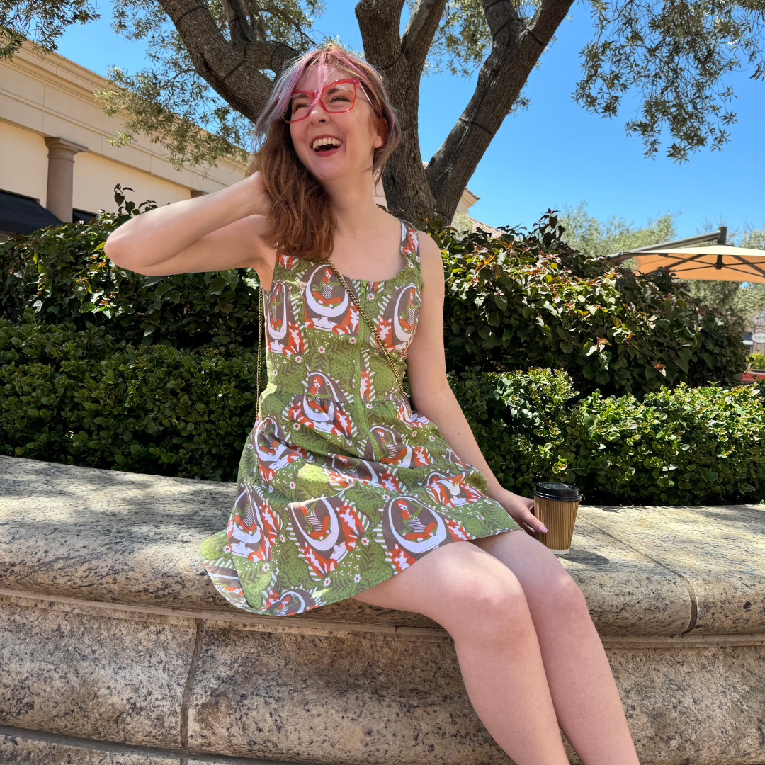 Seated model laughing and wearing olive green ip-front dress with retro print