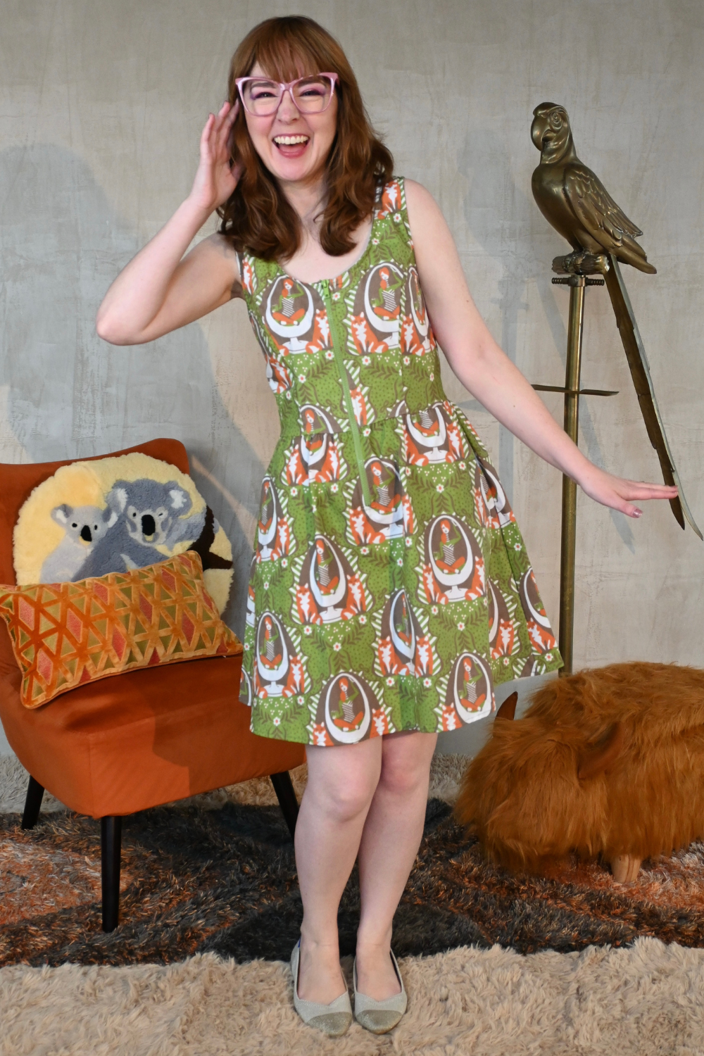 Brown-haired model with pink glasses posing in olive green fox and girl print zip-front knee length dress
