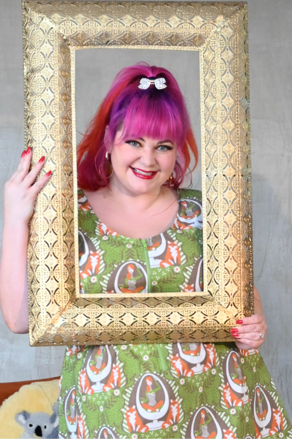 Cute pink-haired model in olive green fox and egg chair print dress, posing with a picture frame
