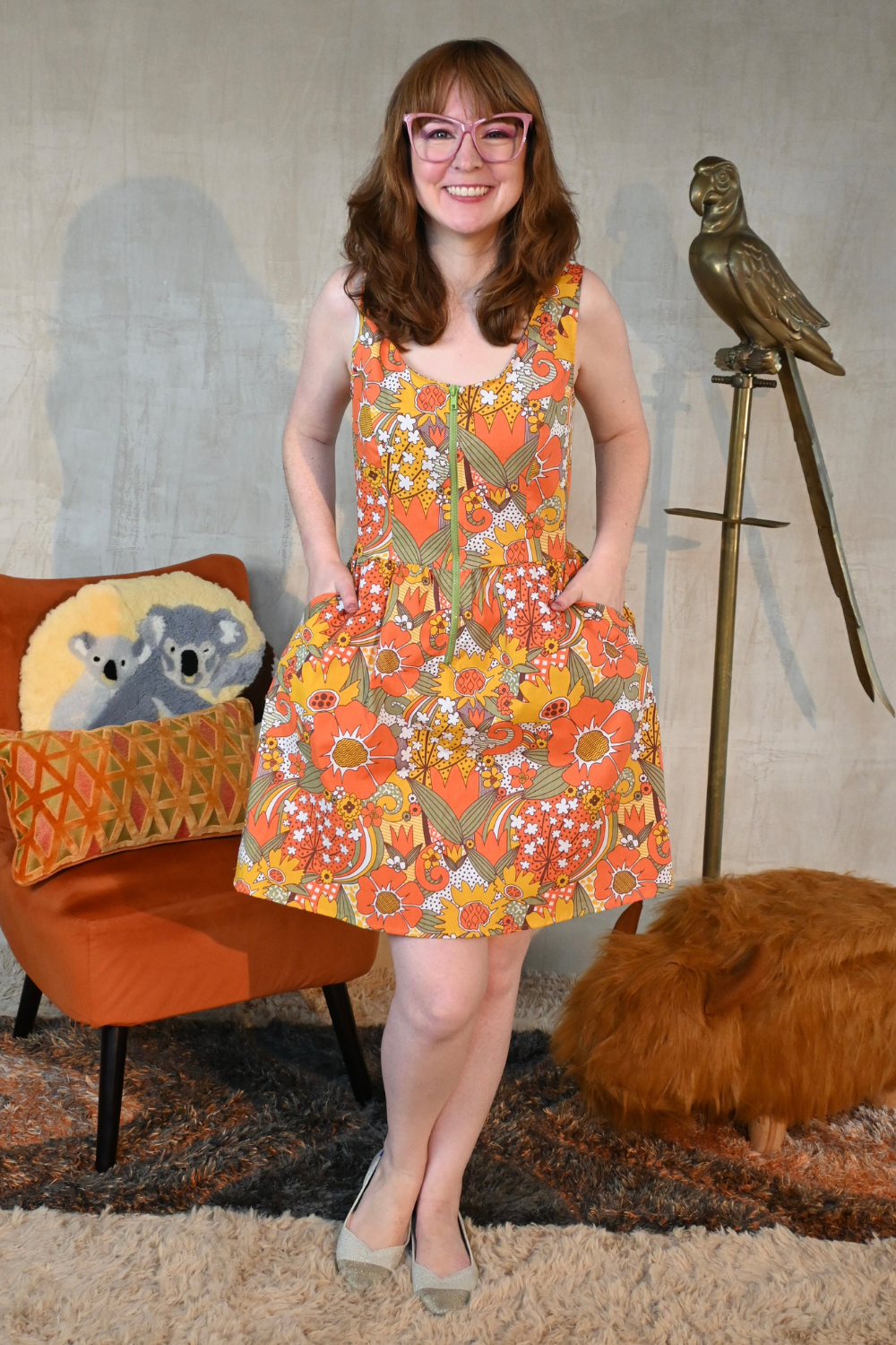 Brown-haired model with glasses wearing fit & flare knee-length floral dress in orange, green and yellow