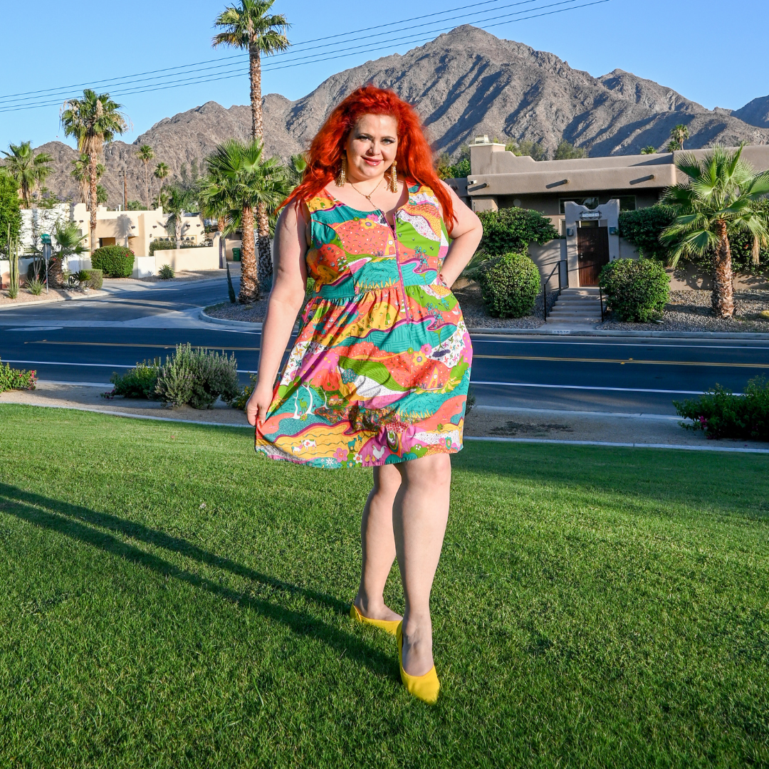 Red-headed model in Palm Springs wearing brightly colored landscape print sun dress