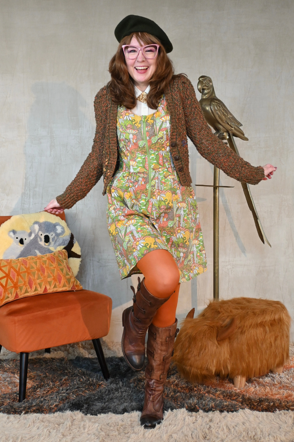 Dancing brown-haired girl wearing mushroom print layered with cute cardigan, tights, boots and a beret in living room
