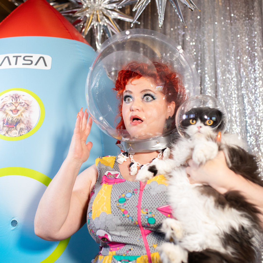 Closeup of model wearing a print of cats driving spaceships and space helmet holding cat wearing space helmet