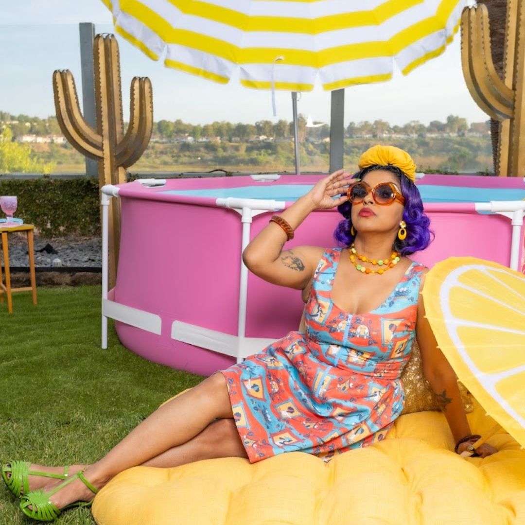 Seated model wearing vintage-inspired fit and flare dress with front zip and colorful print