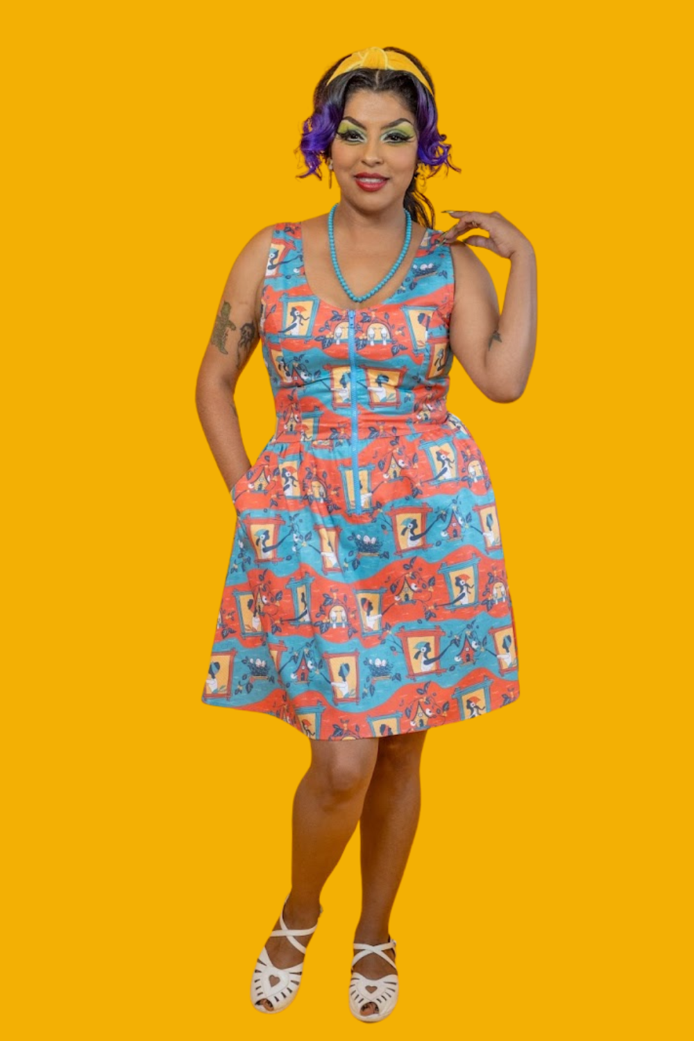 Model in red, yellow and blue fit and flare dress featuring vintage inspired print of ladies and birdhouses