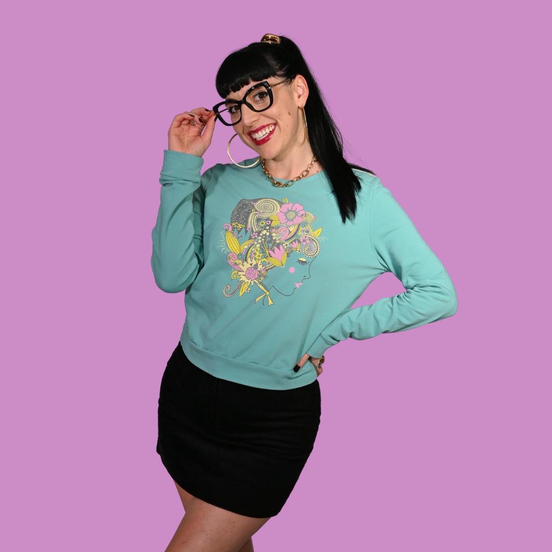 Woman wearing a teal sweatshirt with a colorful graphic design on a purple background