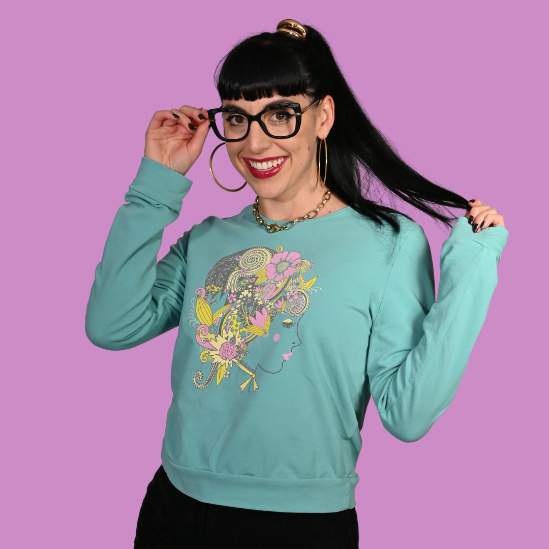 Woman wearing a teal sweatshirt with a colorful design against a purple background
