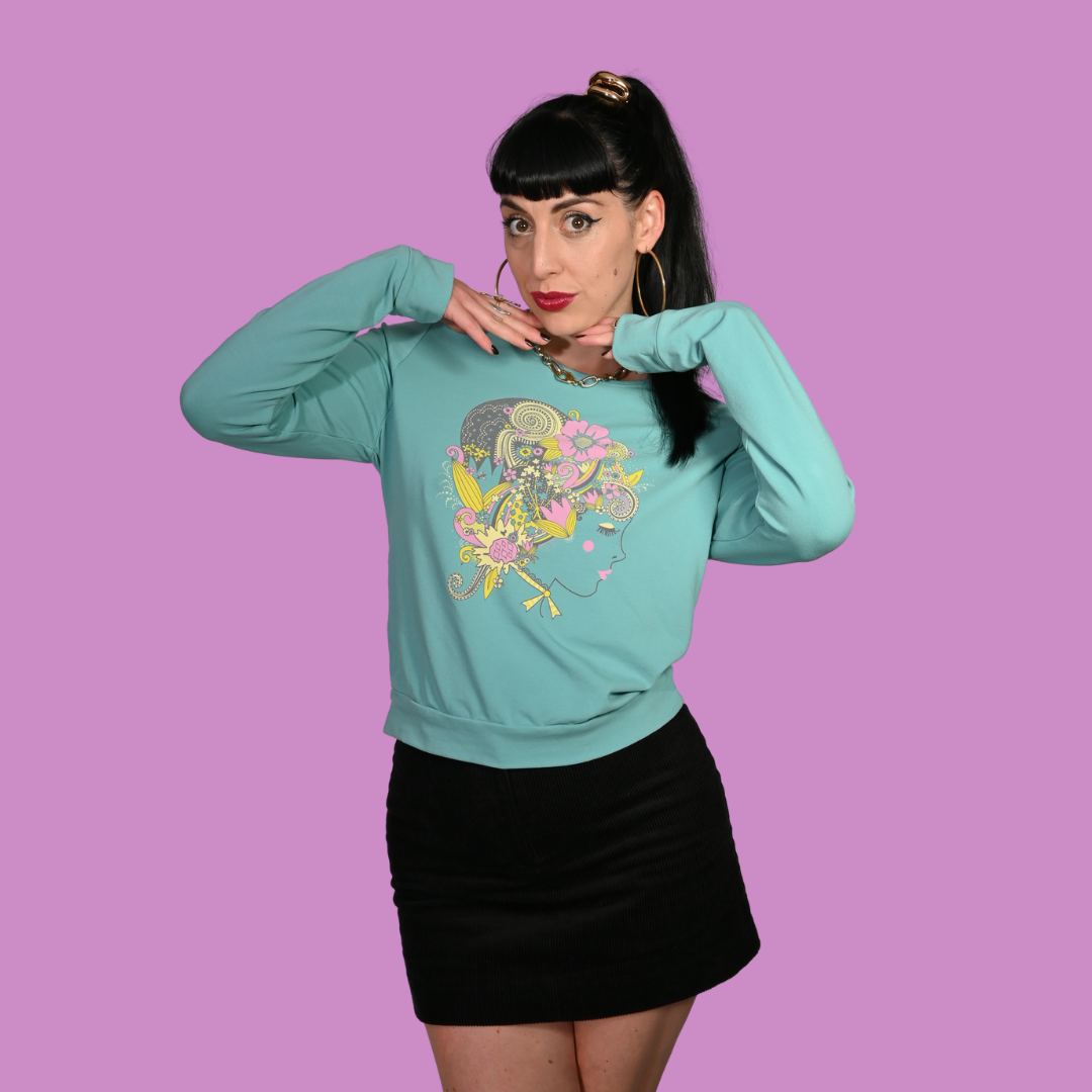 Woman wearing a teal sweatshirt with a colorful graphic design on a purple background