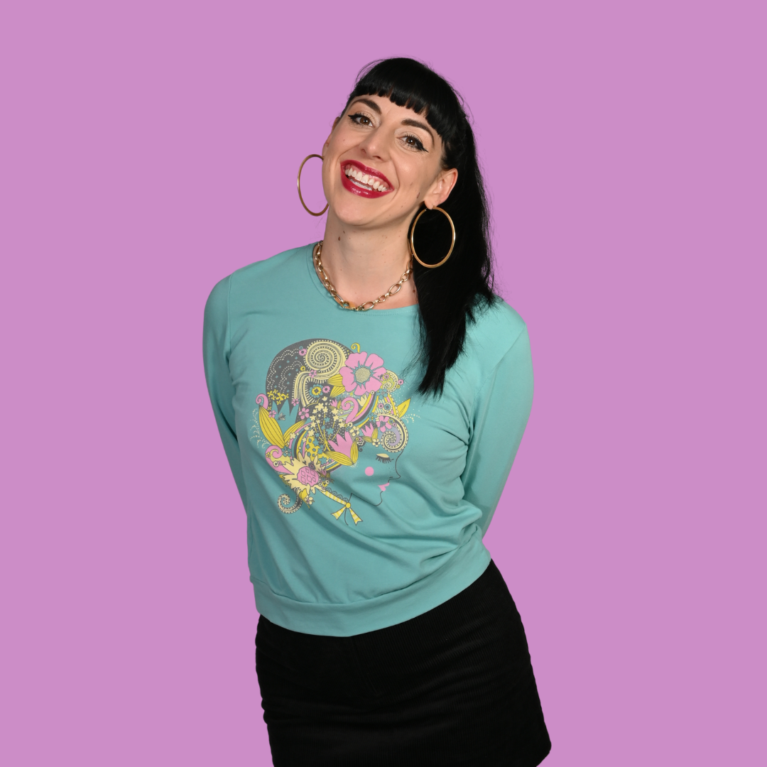 Woman wearing a teal sweatshirt with a vintage-inspired graphic design on a purple background