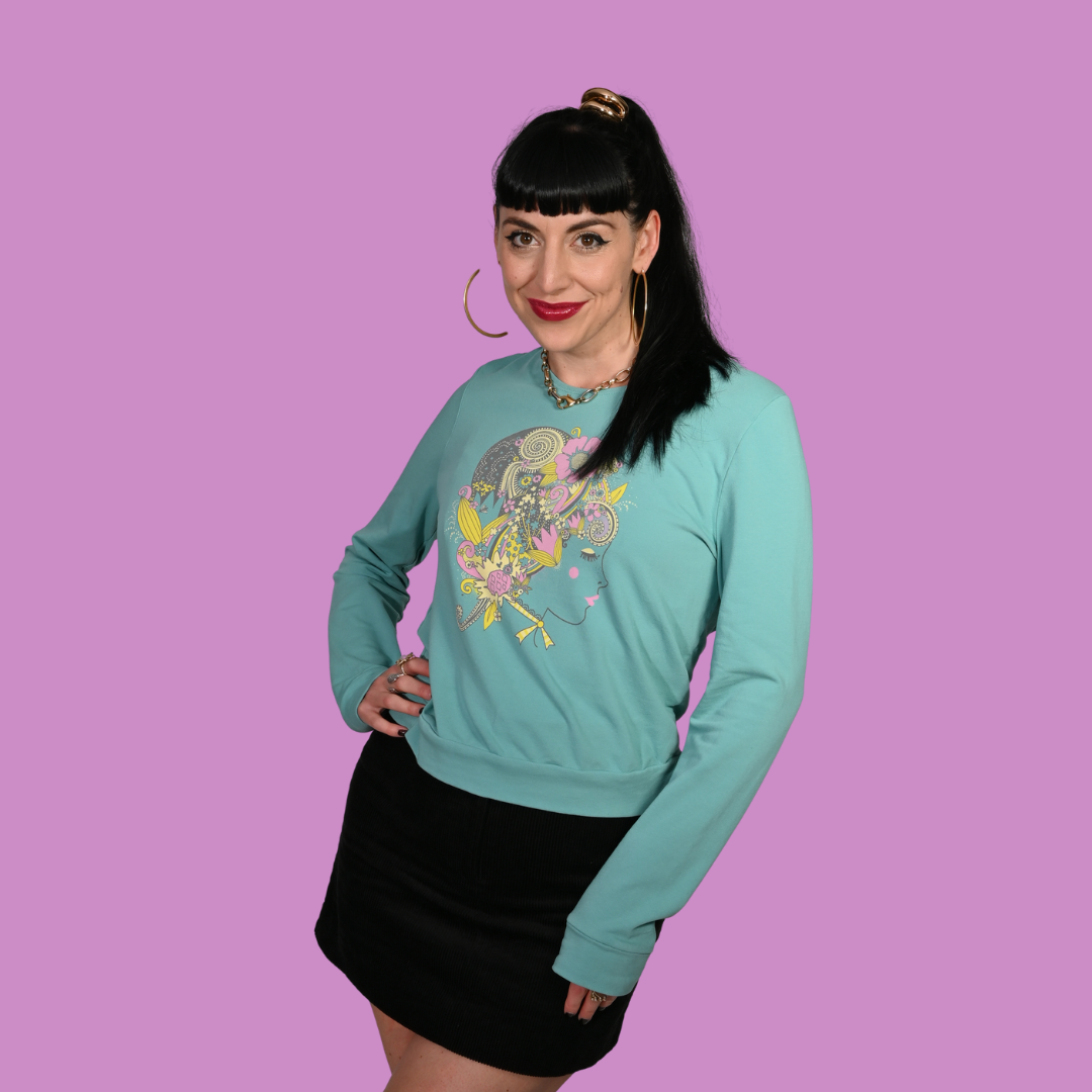 Woman wearing a light blue sweatshirt with a colorful graphic design on a purple background