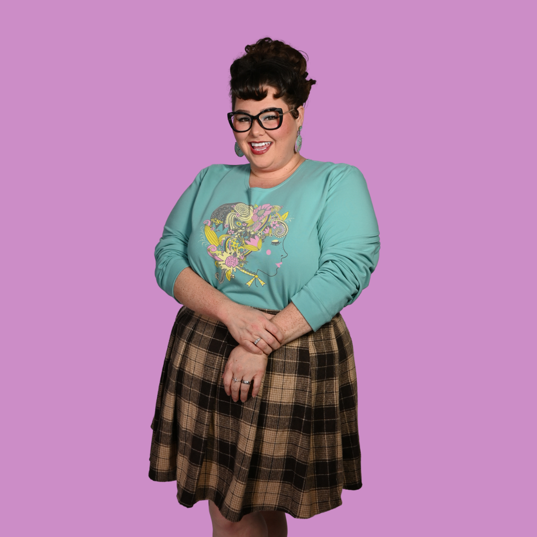 Person wearing a teal sweater with a colorful design and a plaid skirt on a purple background