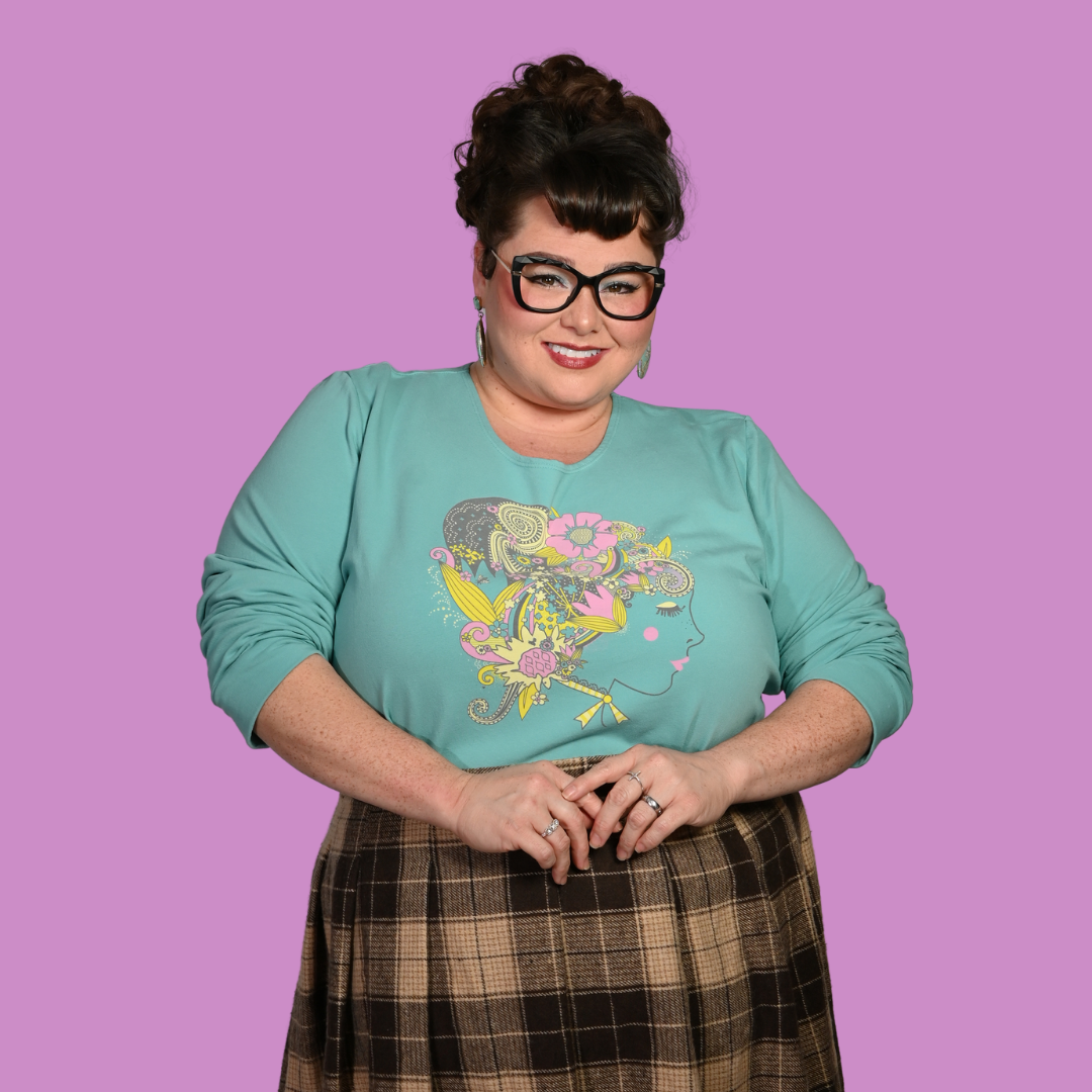 Person wearing a teal shirt with a colorful design and plaid skirt on a purple background