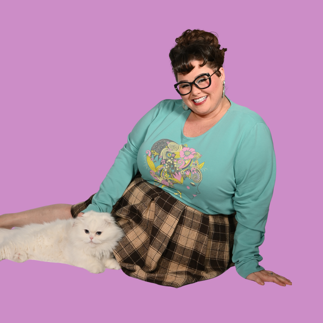 Dark-haired  woman wearing a teal shirt with a graphic design and plaid skirt, sitting on a purple background with a white cat.