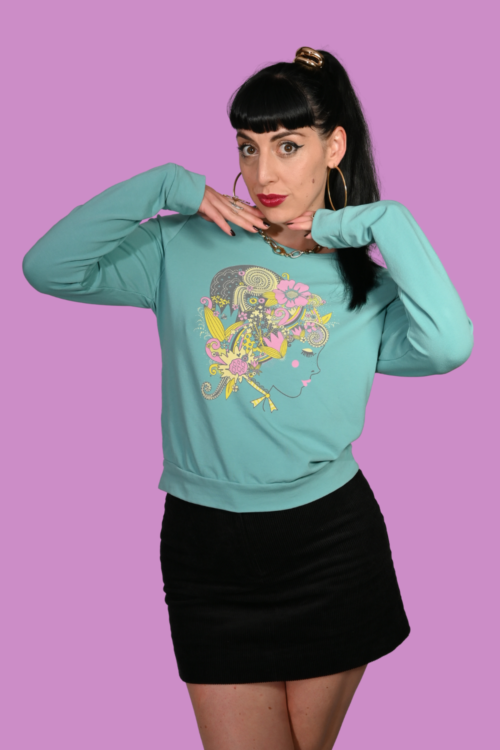 Woman wearing a teal sweatshirt with a colorful graphic design on a purple background