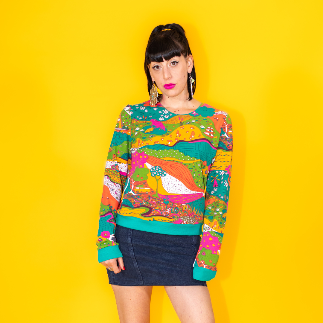 Black haired model with bright lipstick and wearing fun landscape print sweatshirt in bold colors and denim miniskirt