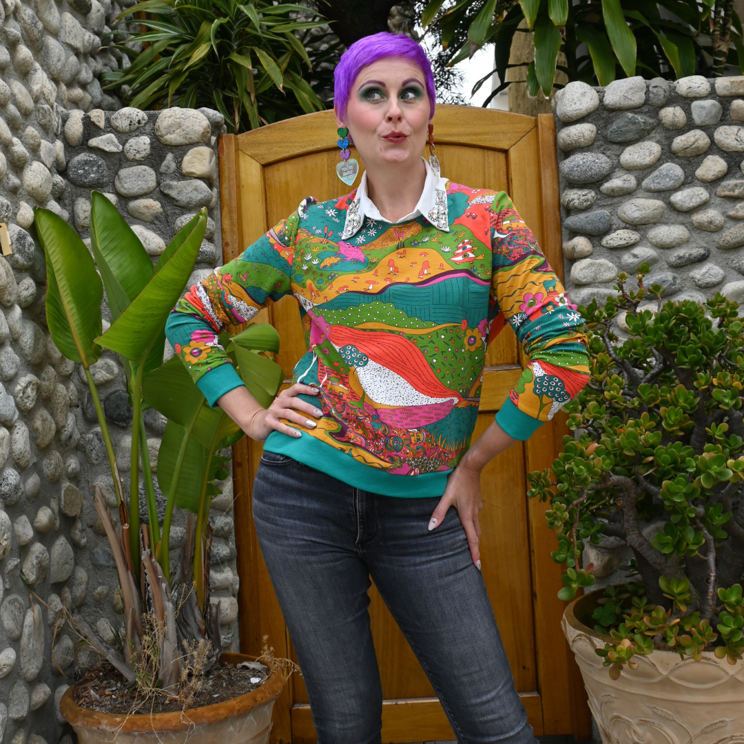 Pretty model in bright colored printed sweatshirt and black pants in front of pretty natural backdrop