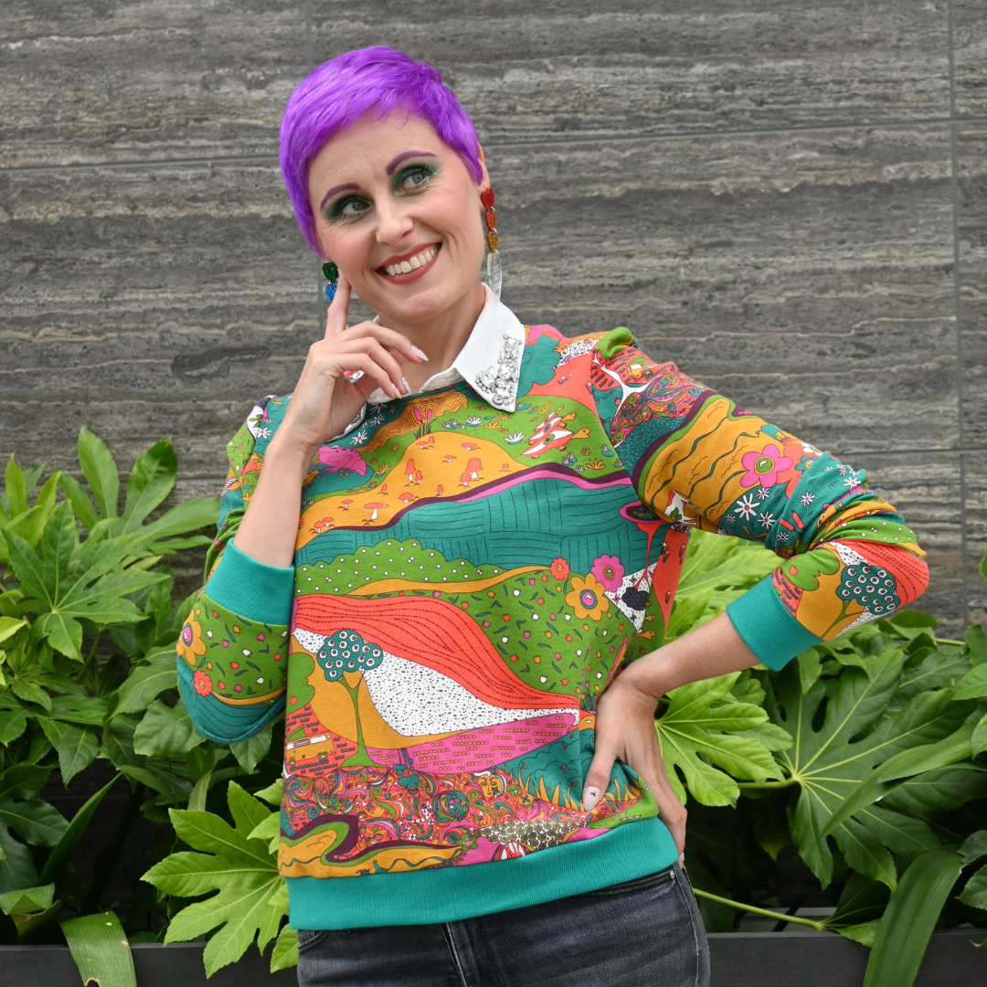 Purple-haired model in bright colored printed sweatshirt and black pants