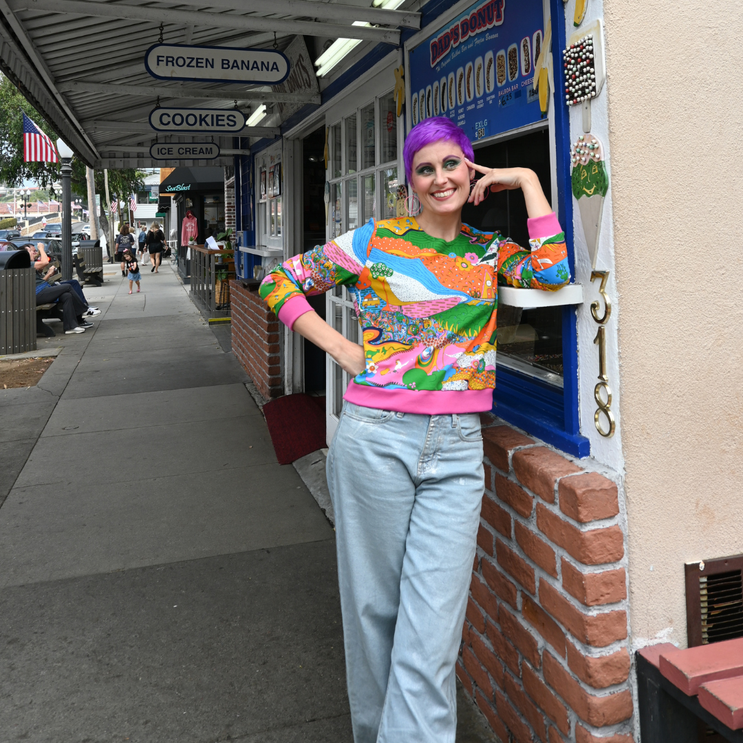 Cute model in rainbow farm yard sweatshirt & leaning against a frozen banana stand