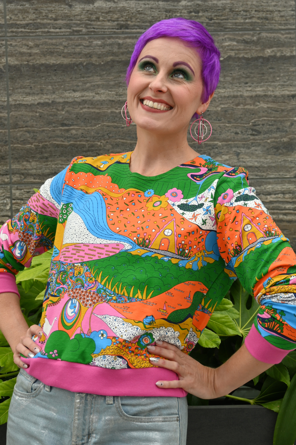 Purple-haired model in rainbow printed sweatshirt and jeans