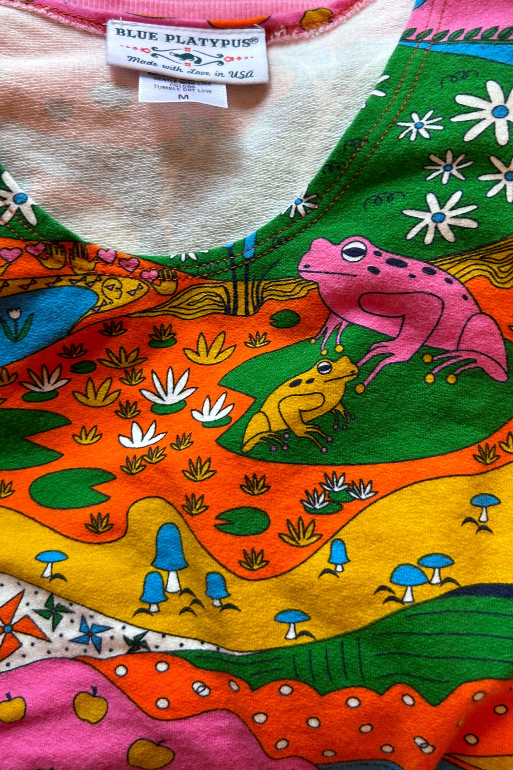 Closeup of neck of sweatshirt featuring frogs, mushrooms and lily pads
