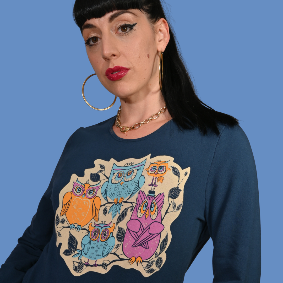 Closeup of woman wearing a navy blue sweatshirt with colorful owl design against a blue background