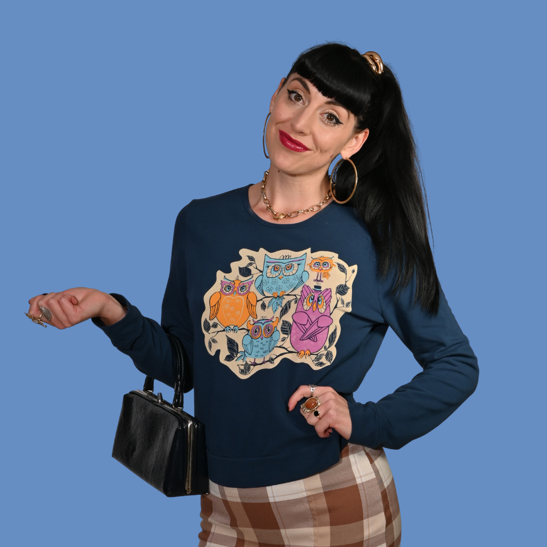 Woman wearing a navy blue sweater with colorful owl design against a blue background