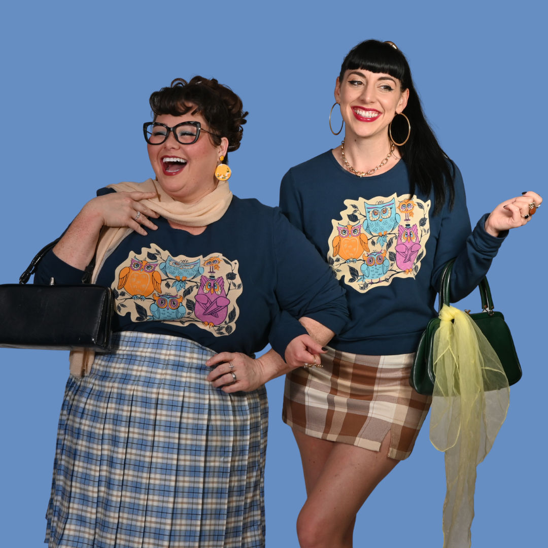Two women wearing matching sweatshirts with owl designs against a blue background