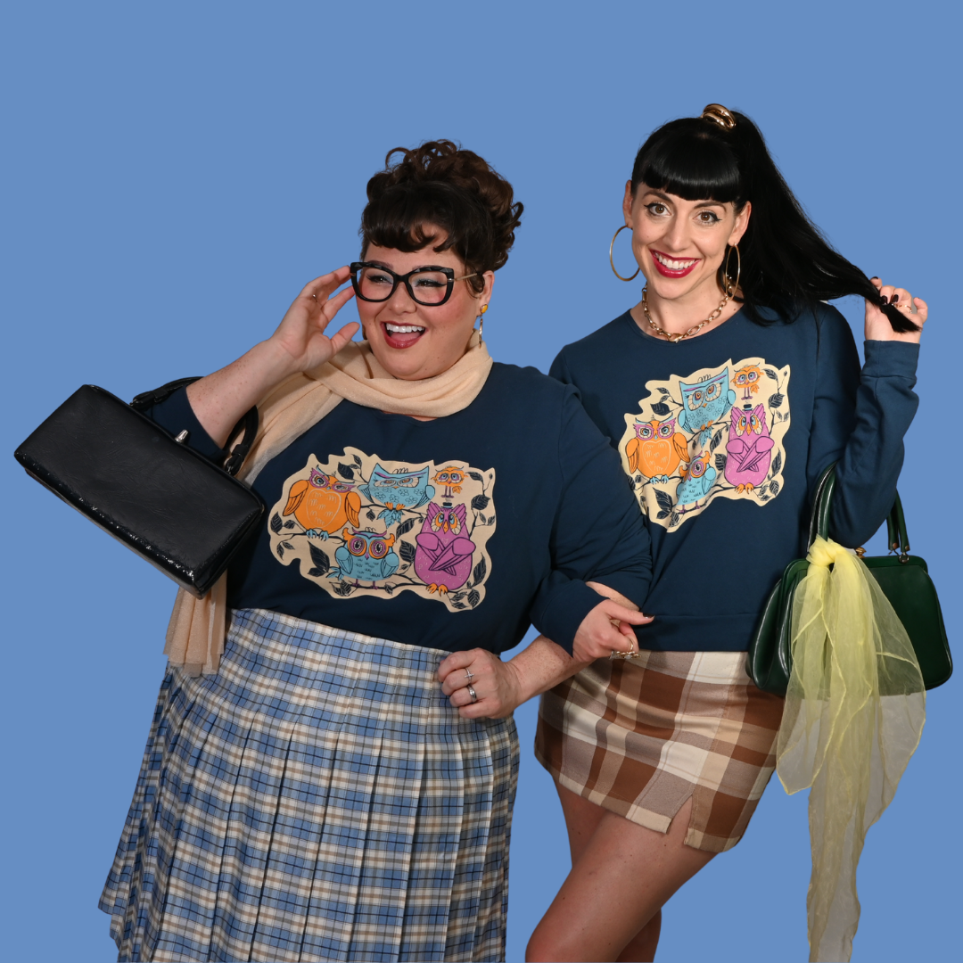 Two women wearing matching sweatshirts with colorful designs against a blue background