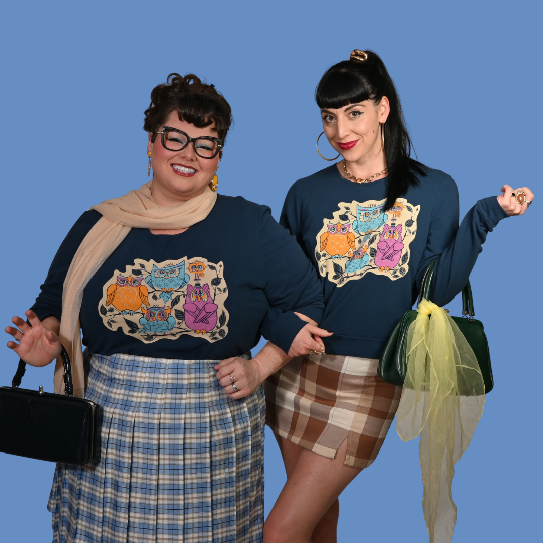 Two women wearing matching French terry pullovers with cat designs against a blue background