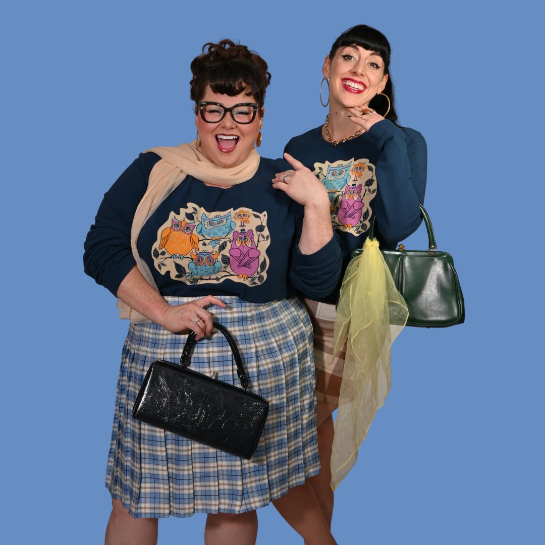 Two women wearing matching outfits with colorful owl print weatshirts and plaid skirts, holding handbags against a blue background.