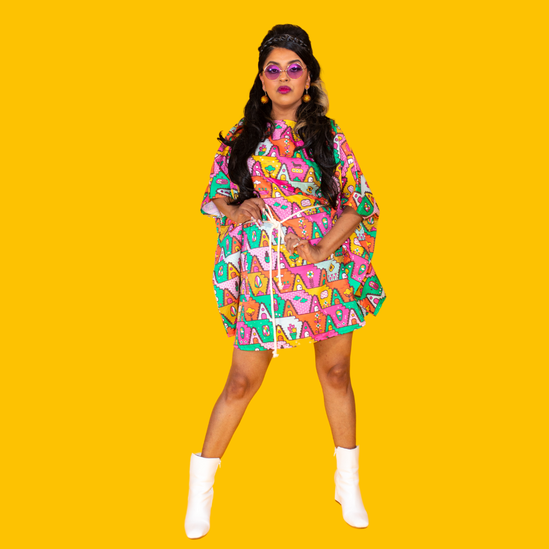 Latina model with long hair and brightly colored mini muumuu beach dress and boots and round sunglasses