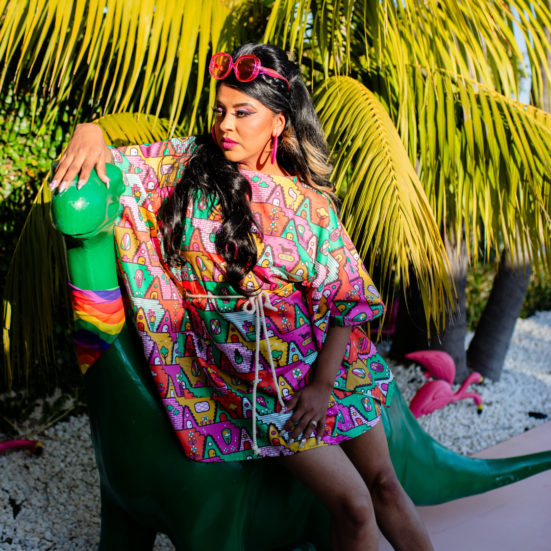 Latina model with long hair and brightly colored mini muumuu beach dress and boots, on toy dinosaur