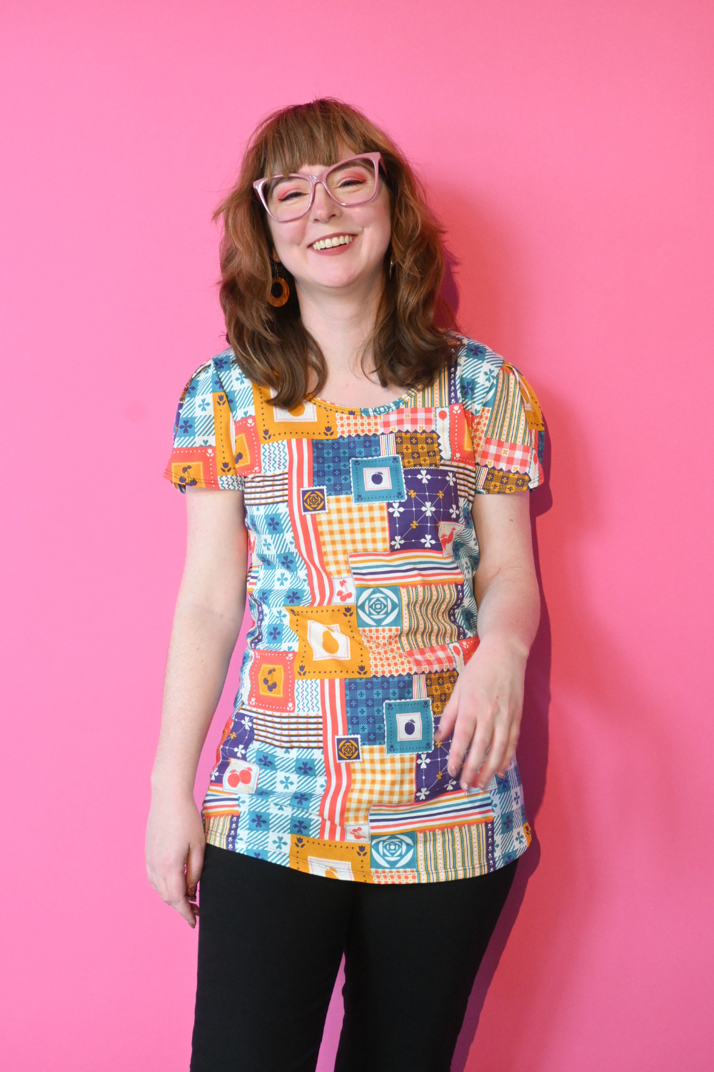Brown-haired model with glasses wearing patchwork print shirt in primary colors