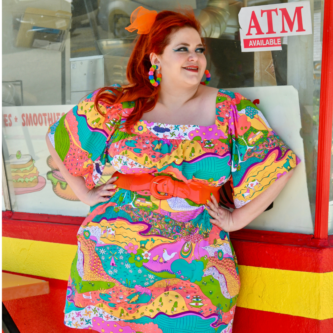 Red-haired model in brightly colored printed dress and fun accessories, in front of donut shop window