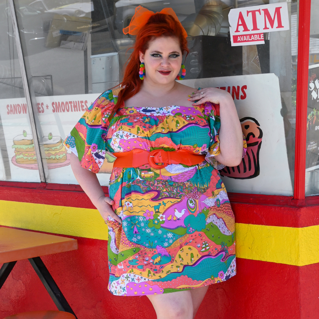 Red-haired model in brightly colored printed dress and fun accessories, in front of donut shop