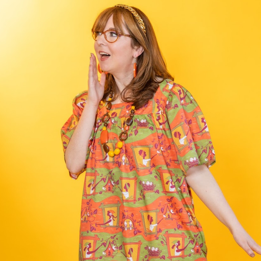 Closeup of model in cotton girl and bird print dress in orange and green