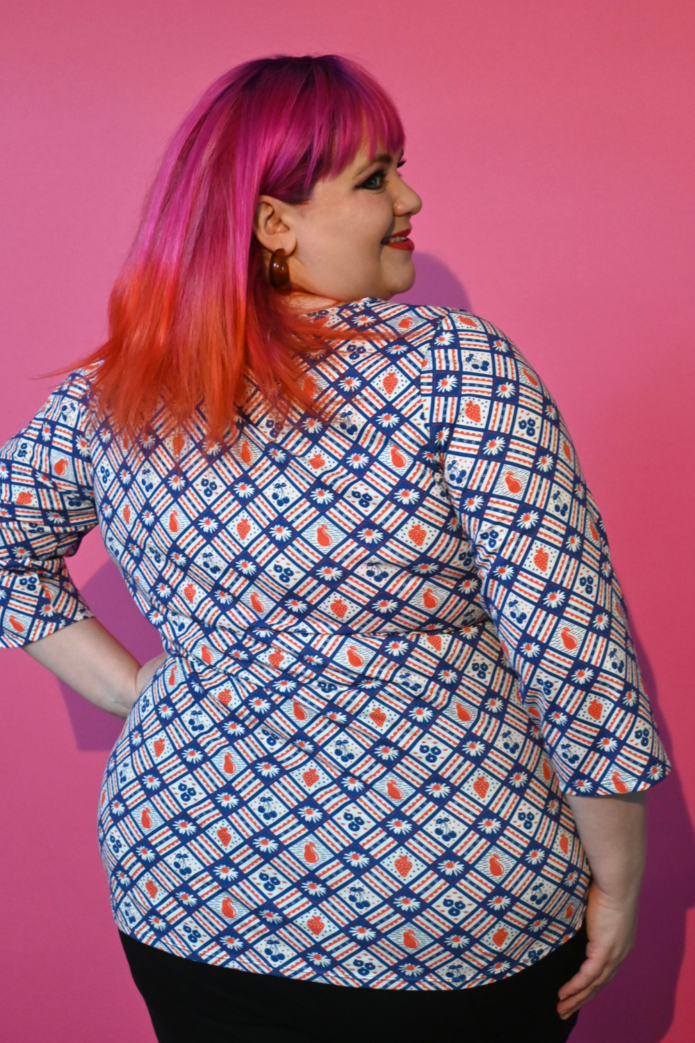 Back view of pink-haired model in floral and fruit print 3/4 sleeve tee