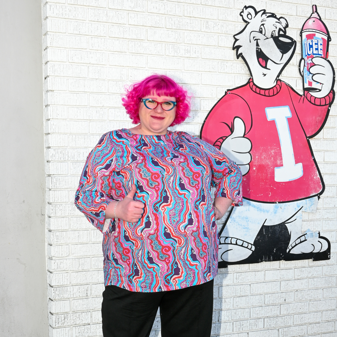 Pink-haired model in swirling psychedelic print tee with slushie mural in the background