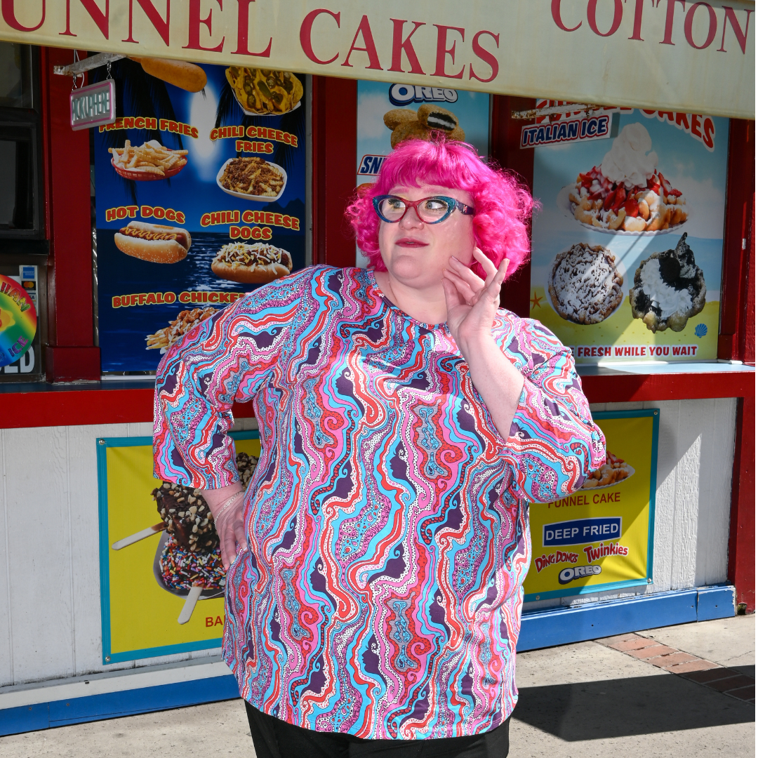 Pink-haired model in swirling psychedelic print tee in front of food stand