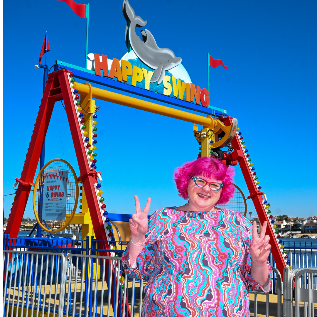 Pink-haired model in swirling psychedelic print tee giving peace signs at the carnival