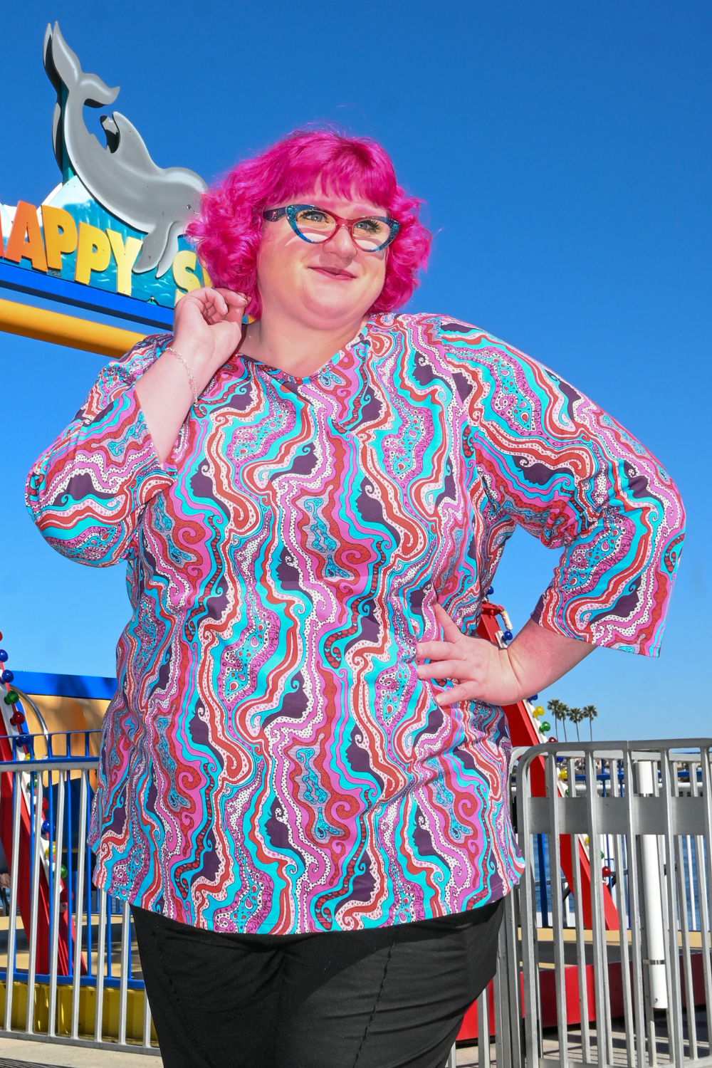 Pink-haired model in swirling psychedelic print tee at the carnival