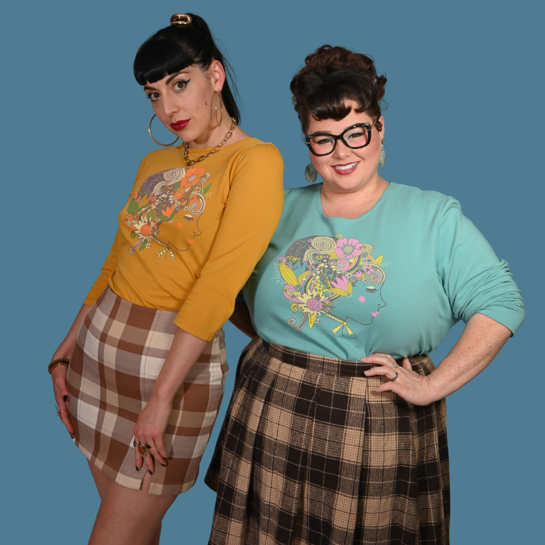 Two women wearing matching outfits with plaid skirts and colorful shirts against a blue background